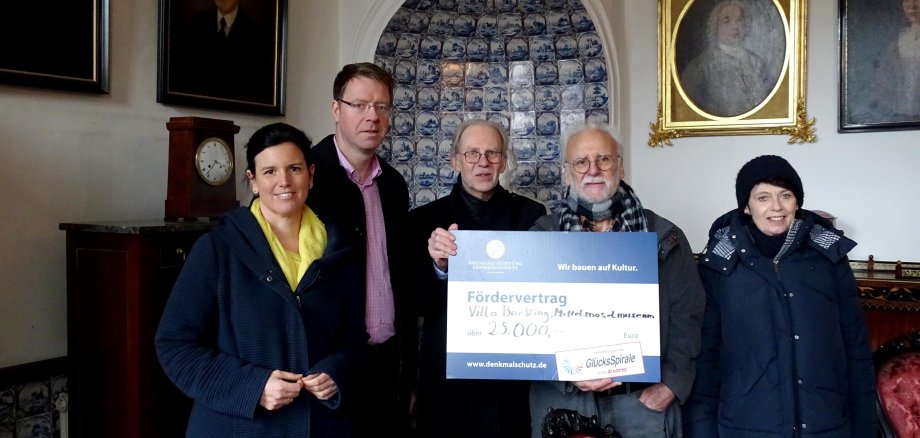 An dieser Stelle ist ein Bild von dem Bürgermeister Marcus Heintel, Patrice Langer, Erich Engelke und Thomas Kirsch, wie sie in der Villa Böcking stehen und den 25000€ Check halten.