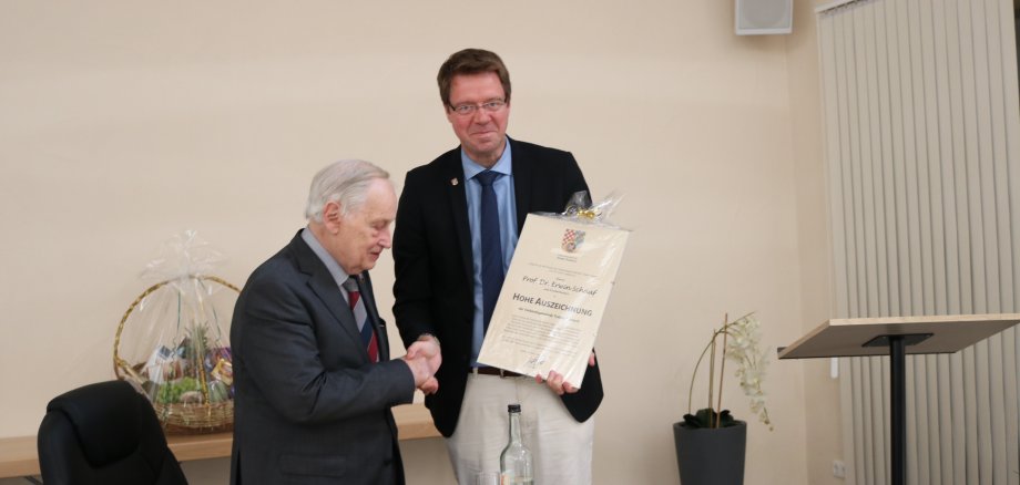 An dieser Stelle ist ein Foto von Bürgermeister Marcus Heintel wie er Prof. Dr. Erwin Schaaf die Urkunde überreicht und sich beide die Hände schütteln.