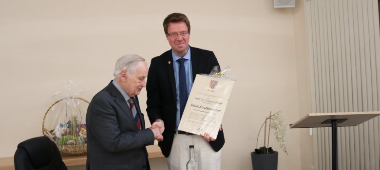 An dieser Stelle ist ein Foto von Bürgermeister Marcus Heintel wie er Prof. Dr. Erwin Schaaf die Urkunde überreicht und sich beide die Hände schütteln.